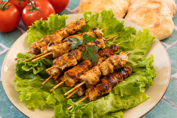 grilled chicken skewers on lettuce leaves , fresh ripe tomatoes and bread on table