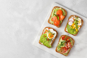 Variety of Healthy sandwiches, set of toasts with avocado. Slice of whole grain dark bread with avocado, cream cheese, tomatoes, radishes, salmon, eggs, hamon.