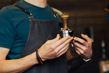 Barista carefully presses ground coffee using tamper for preparing the coffee.