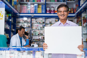 happy customer sytanding in front of medical shop by holding white empty signs board by looking at...