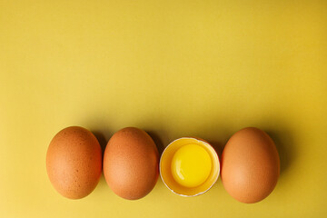 Fresh brown eggs and a broken egg with yolk on a light yellow background with space for text, copy space