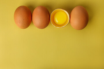 Fresh brown eggs and a broken egg with yolk on a light yellow background with space for text, copy space