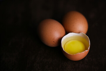 Fresh brown eggs and a broken egg with yolk on a dark wooden background