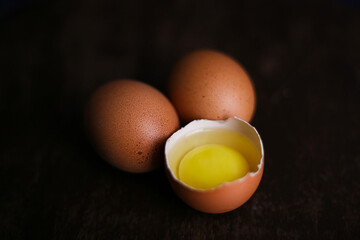 Fresh brown eggs and a broken egg with yolk on a dark wooden background