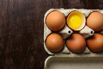 Fresh brown eggs and a broken egg with yolk in an eco tray made from recycled paper on a dark wooden background