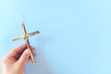 Top view of hand holding wooden cross crucifix with copy space in blue background. Catholicism,...