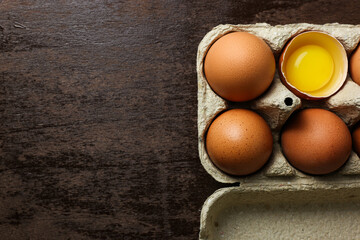 Fresh brown eggs and a broken egg with yolk in an eco tray made from recycled paper on a dark wooden background