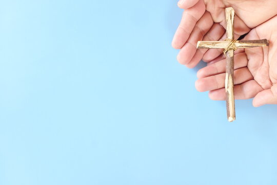 Top view of hand holding wooden cross crucifix with copy space in blue background. Catholicism, Christianity, Thanksgiving, Catholic and Christian faith concept.