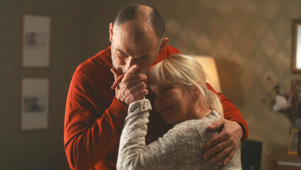 Happy senior man and woman in marriage smiling and funny dancing together in a cozy living room