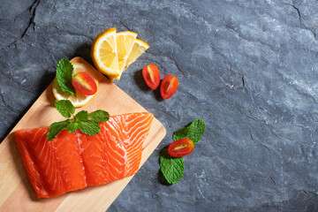 Salmon. Fresh raw salmon fish. Raw salmon fillet with pepper, herbs, lemon, tomato ingredients for cooking on black stone table rustic style. Top view with copy space.