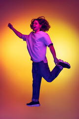 Full-length portrait of young excited man jumping isolated on orange background in neon light, filter. Concept of emotions, beauty, fashion