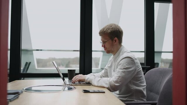 adult man is working alone in modern office, using laptop with wireless internet connection for searching information