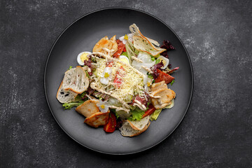 Caesar salad with chicken, on a black plate
