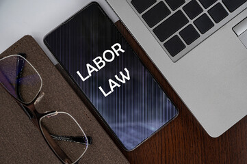 Top view of phone on table near laptop, notepad and glasses with inscription labor law.