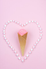 Pink ice cream in a waffle cone in a marshmallow heart on a pink background.