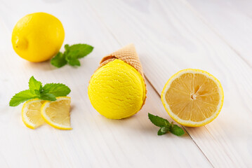 Yellow ice cream with lemon and mint in a waffle cone on a white wooden table.