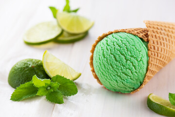 Green ice cream with lime and mint in a waffle cone on a white wooden table.