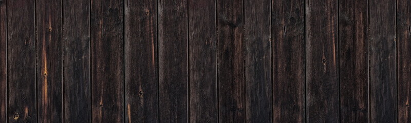 Old blacked knotty wooden board wide banner texture. Aged rough dark wood plank fence large background. Dark rustic widescreen backdrop