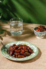 Dried dates in a green vintage plate on a brown textile background. Rustic style