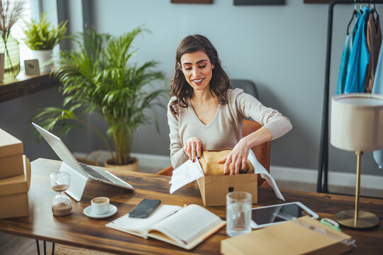 Excited caucasian young woman sit on chair at home unpack cardboard box shopping online, overjoyed black millennial girl buyer feel euphoric open shipped package parcel from delivery service