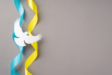 Stop the war in Ukraine concept. Top view photo of national flag curly ribbons and white dove silhouette on isolated grey background with copyspace