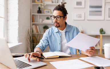 Serious black businessman using laptop and doing paperwork - 495916684