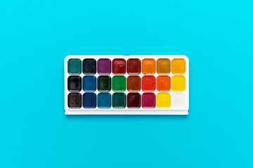 Minimalist photo of watercolor palette on turquoise blue background. Set of watercolor paint with central composition.