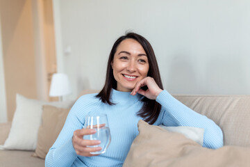 beautiful happy asian woman holding drinking water from glass on the sofa