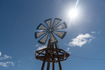 Plano detalle de un molino de viento de madera con pequeñas aspas blancas y azules con el cielo azul de fondo y un sol brillante. Punta Mujeres, Lanzarote