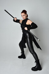 Full length portrait of pretty red haired female model wearing black futuristic scifi leather...