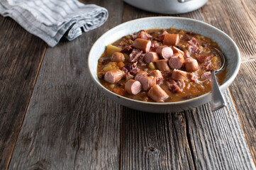 Pork stew with vegetables, potatoes, beans and boiled sausage in a bowl with spoon