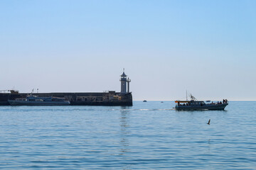 A tranquil seascape. Small pleasure boats on the background of the white tower of the old lighthouse. Yalta, Crimea.