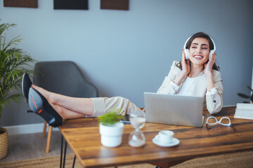 A smiling black-haired woman with headphones and a laptop looking at the screen, a happy young...