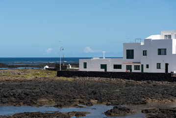 Vista del pueblo Orzola en Lanzarote, Islas Canarias, con su tradicional arquitectura de pequeñas casas de color blanco durante un día soleado con el cielo azul despejado y la marea baja. 