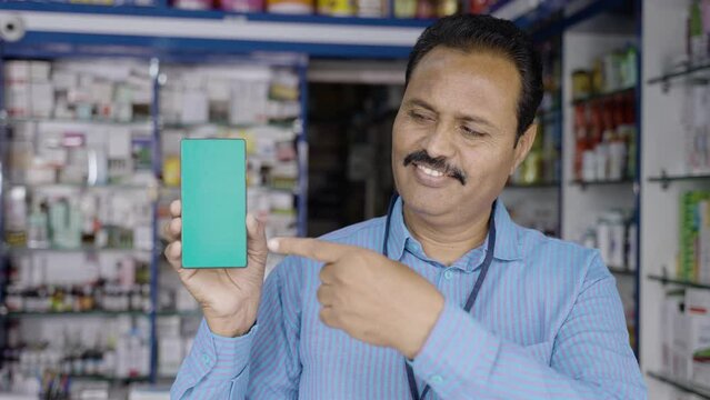 smiling medical shop owner showing green screen mobile phone by looking at camera - concept of epharmacy, making online order,app advertisement and promotion.