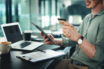 Fototapeta premium Technology makes payments quick and easy. Shot of a young businessman holding a credit card while using a digital tablet in an office.