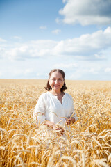 Naklejka na ściany i meble Elderly woman in white walking through wheat field.