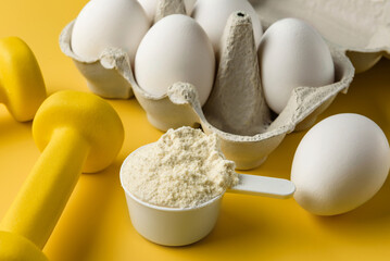 A scoop of egg white, a pair of dumbbells, and a carton of eggs. The concept of sports nutrition.
