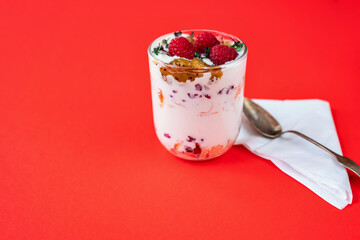 Coconut mousse with raspberry and kiwi jam, white napkin and spoon on red background.