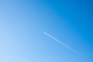 An airplane is dragging a contrail behind it. A bright blue sky on a summer day with a plane. Background photo with a clear blue sky. Aircraft with a straight white line of the condensation trail.