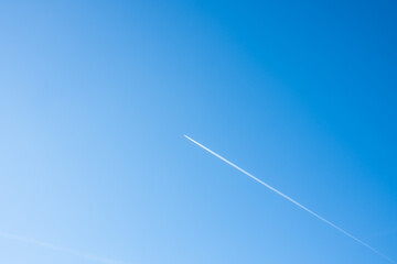 An airplane is dragging a contrail behind it. A bright blue sky on a summer day with a plane....