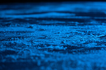 Ice background and texture with scratches from skating and hockey. Ice rink floor, detail of textured ice background with snow and crystals in blue light. Empty ice rink close up.