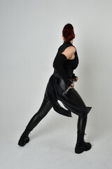 Full length portrait of pretty redhead female model wearing black futuristic scifi leather costume,...