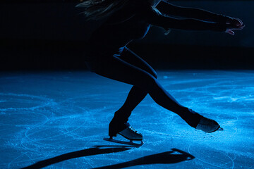 Figure skating lady is wearing black sportswear is skating on ice rink, training at night in the rays of blue light. Young woman preparing to competition, training rotation and slides skills. Close up © kinomaster