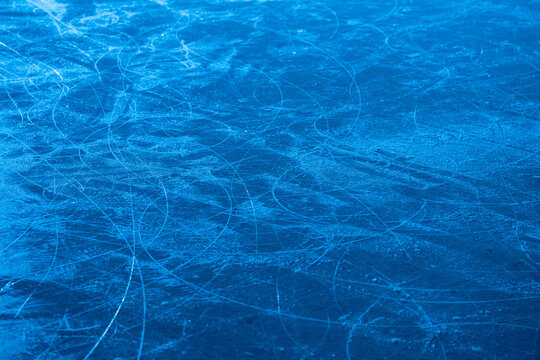 Ice surface in sports arena for figure skating or hockey. Ice background and ice texture is cut with pattern and scratches from skates. Detail of textured ice with snow in blue light. Close up.