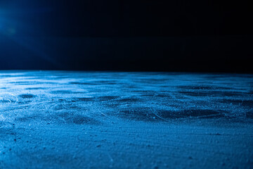 Low angle on ice surface in arena for figure skating or hockey. Ice background and ice texture is cut with pattern and scratches from skates. Detail of textured ice with snow in blue light. Close up.