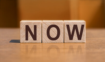 Word NOW on wooden cubes on orange background.