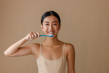 Cheerful Asian woman brushing teeth in studio