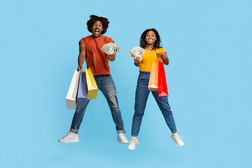 Rich black couple with purchases and banknotes jumping on blue