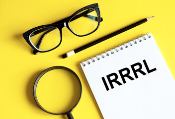 Notepad with IRRRL note on yellow desk with glasses, pencil and magnifier. IRRRL - Interest Rate Reduction Refinance Loan.